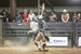 Cowboy riding a bull with others looking on behind the bucking shoots