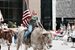 Woman riding a longhorn and carrying an American flag during a parade